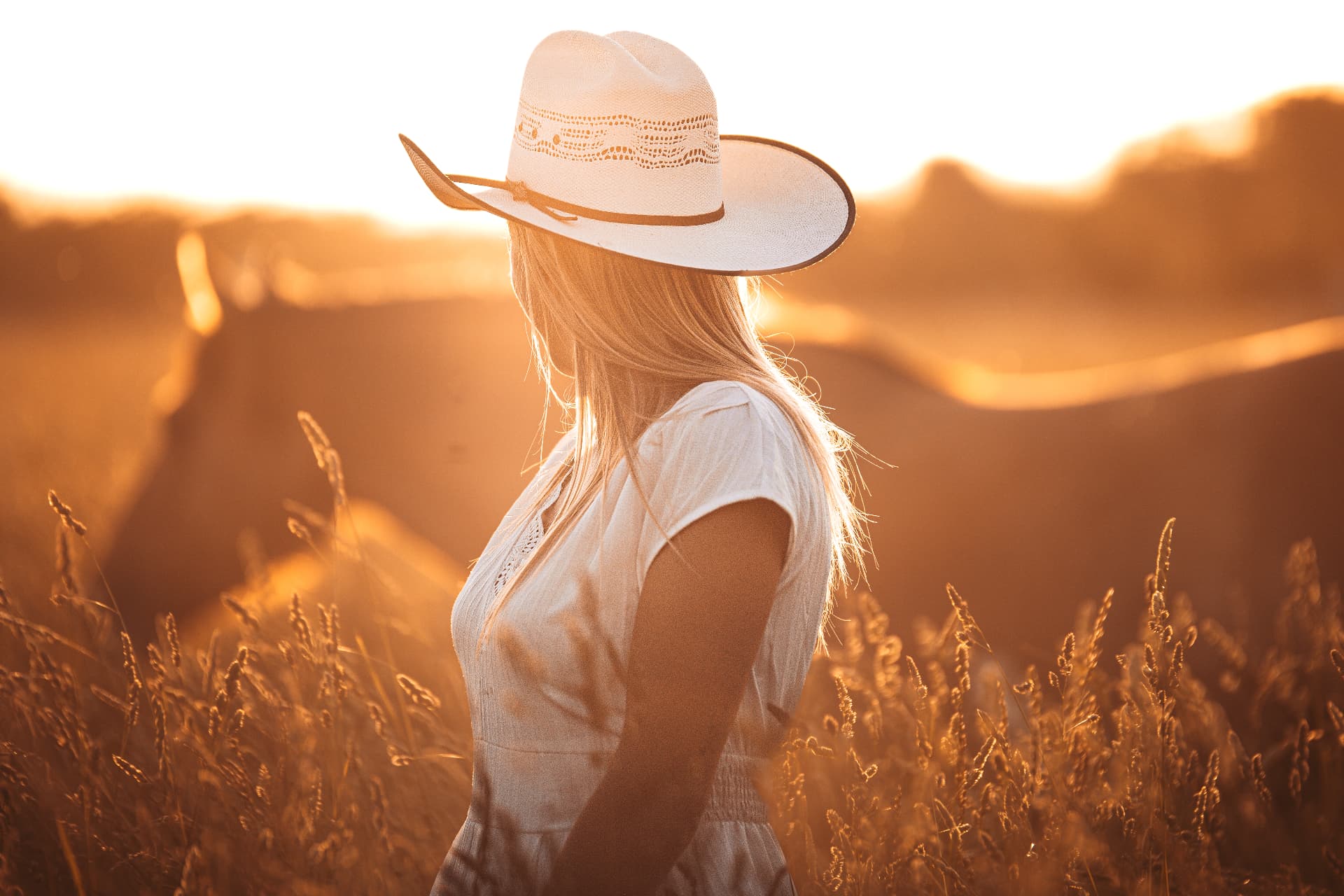 Femme au chapeau dans un champ doré au coucher du soleil